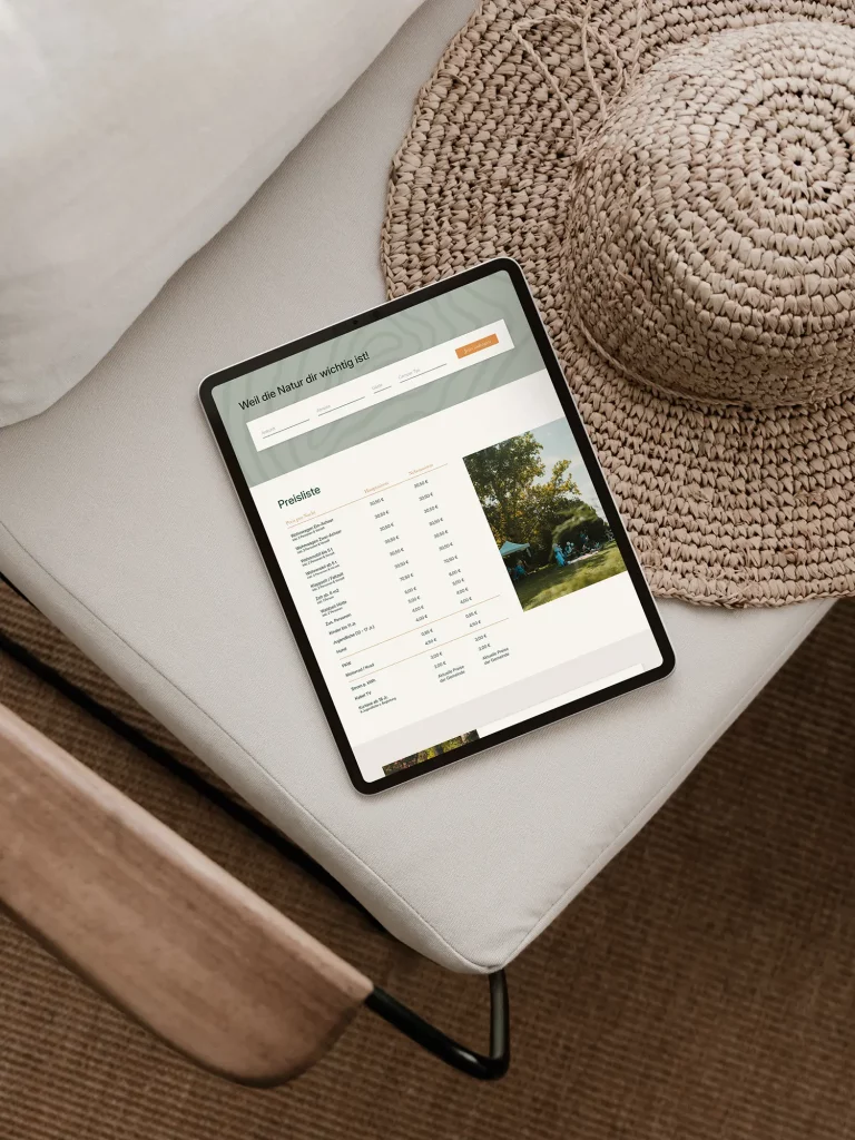 Tablet liegt auf einem hellen Stuhl, daneben ein Strohhut, auf dem Bildschirm eine Preisliste mit der Überschrift „Weil die Natur dir wichtig ist“.